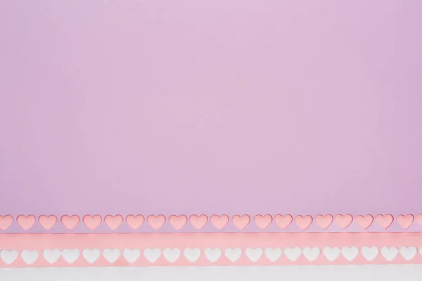 Vue du dessus du papier rose violet avec des coeurs découpés sur fond blanc — Photo de stock