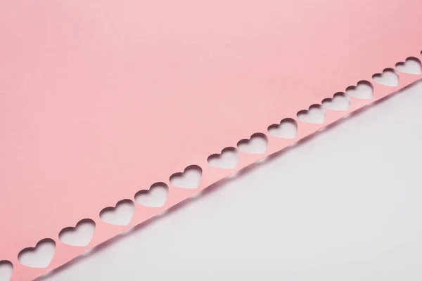 Papier rose avec des coeurs découpés sur fond blanc — Photo de stock
