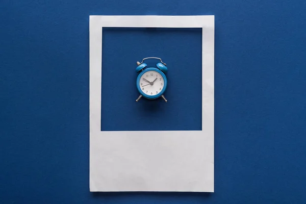 Vista superior del reloj despertador en marco de foto blanco sobre fondo azul - foto de stock