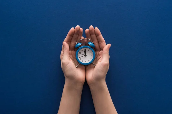 Vista recortada de la mujer que sostiene el reloj despertador sobre fondo azul - foto de stock