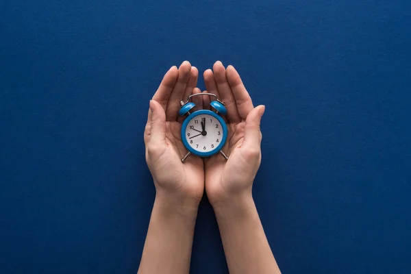 Corte vista de mulher segurando despertador no fundo azul — Fotografia de Stock