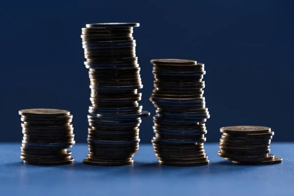 Pilhas de moedas de metal na sombra no fundo azul — Fotografia de Stock