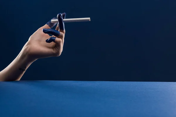 Обрізаний вид жіночої руки з пофарбованими пальцями, що тримає сигарету ізольовано на синьому — стокове фото