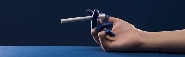 Cropped view of female hand with painted fingers holding cigarette isolated on blue, panoramic shot — Stock Photo