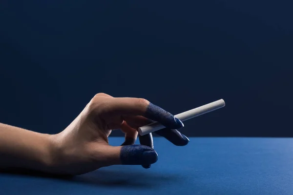 Abgeschnittene Ansicht der weiblichen Hand mit bemalten Fingern, die Zigarette isoliert auf blau halten — Stockfoto