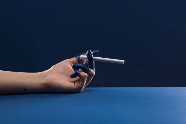 Corte da mão feminina com os dedos pintados segurando cigarro isolado em azul — Fotografia de Stock