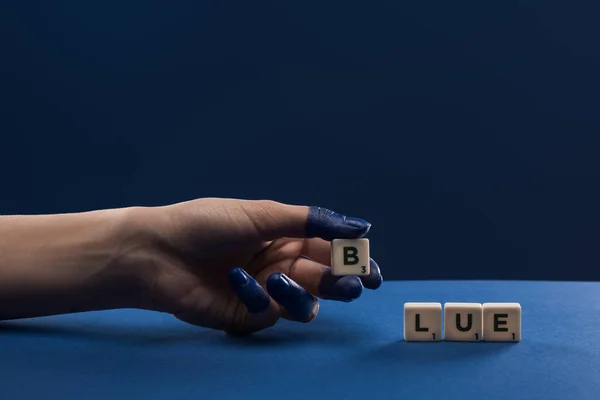 Vista cortada da mão feminina com dedos pintados perto de cubos com letras azuis isoladas em azul — Fotografia de Stock