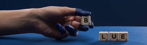 Ausgeschnittene Ansicht einer weiblichen Hand mit bemalten Fingern in der Nähe von Würfeln mit blauer Schrift isoliert auf blauem Grund, Panoramaaufnahme — Stockfoto