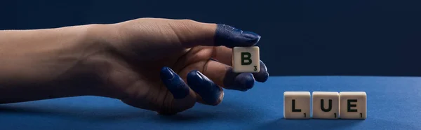 Cropped view of female hand with painted fingers near cubes with blue lettering isolated on blue, panoramic shot — Stock Photo