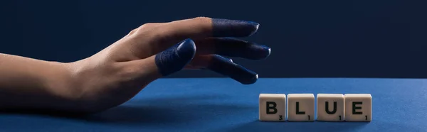 Cropped view of female hand with painted fingers near cubes with blue lettering isolated on blue, panoramic shot — Stock Photo