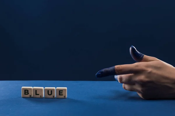 Vue recadrée de la main féminine avec les doigts peints pointant vers les cubes avec lettrage bleu isolé sur bleu — Photo de stock