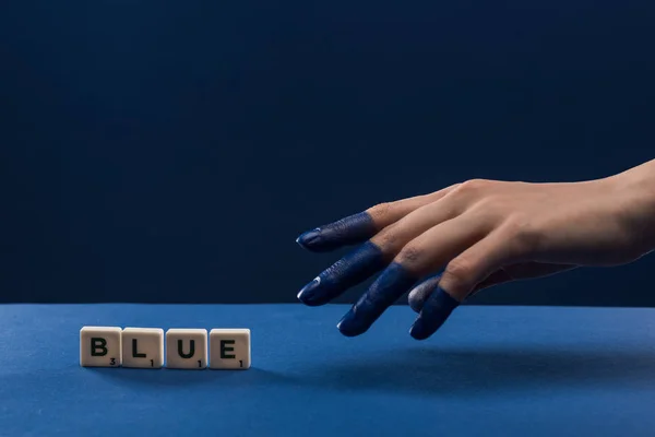 Cropped view of female hand with painted fingers near cubes with blue lettering isolated on blue — Stock Photo