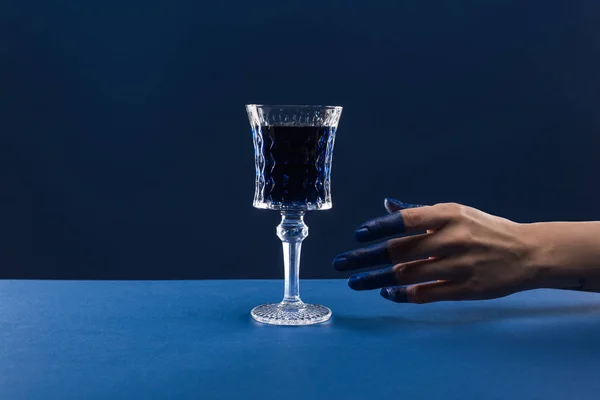 Vue recadrée de la main féminine avec doigts peints près du verre à facettes avec boisson isolée sur bleu — Photo de stock