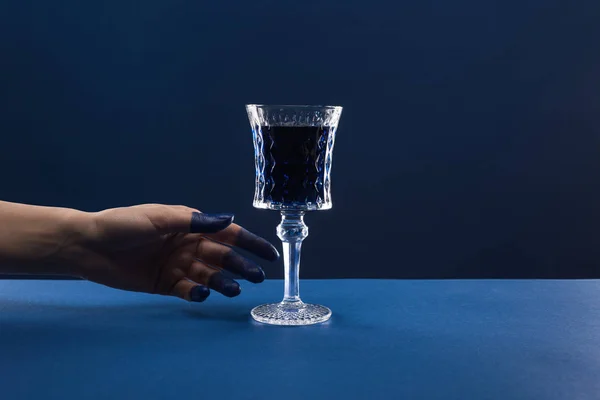 Vue recadrée de la main féminine avec doigts peints près du verre à facettes avec boisson isolée sur bleu — Photo de stock