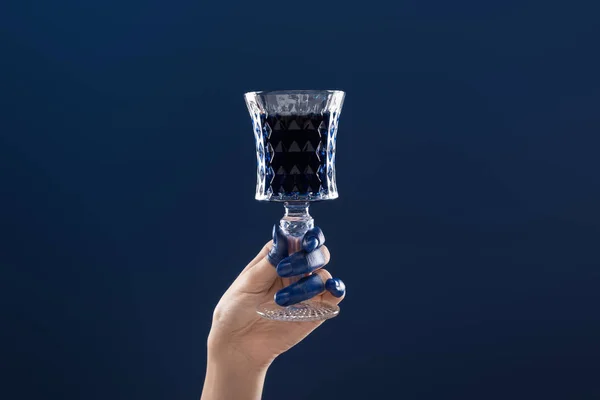 Vue recadrée de la main féminine avec les doigts peints tenant verre à facettes avec boisson isolée sur bleu — Photo de stock