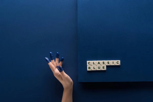 Обрізаний вид жінки з розфарбованими пальцями біля класичної синьої плями на кубиках на синьому фоні — стокове фото
