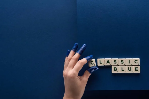 Vista recortada de la mujer con los dedos pintados cerca de letras azules clásicas en cubos sobre fondo azul - foto de stock