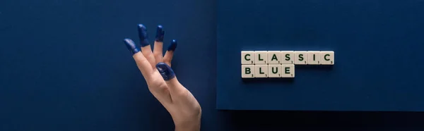 Cropped view of woman with painted fingers near classic blue lettering on cubes on blue background, panoramic shot — Stock Photo