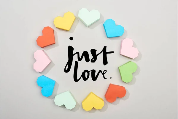 Top view of frame of colorful paper hearts on grey background with just love lettering — Stock Photo