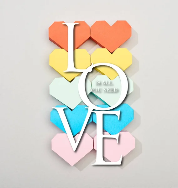 Top view of colorful heart shaped papers on grey background with love is all you need lettering — Stock Photo