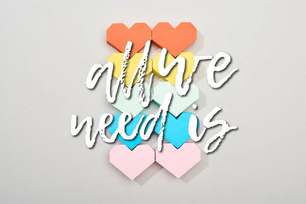 Top view of colorful paper hearts on grey background with all we need is lettering — Stock Photo