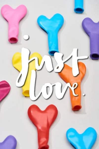 Top view of colorful balloons in heart shape on grey background with just love illustration — Stock Photo