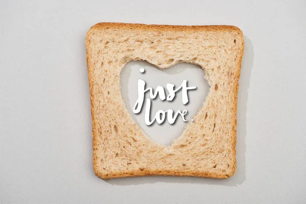 Top view of bread slice with carved heart and just love lettering on grey background — Stock Photo