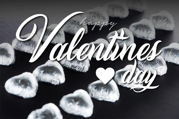 Heart shaped candies in foil on black background with happy valentines day illustration — Stock Photo