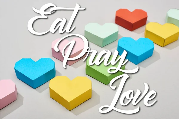 Corazones decorativos multicolores sobre fondo gris con ilustración de comer, rezar, amar - foto de stock