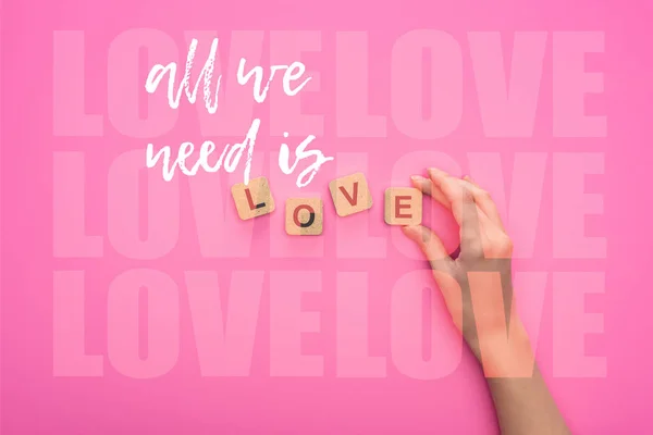 Partial view of woman holding cubes with all we need is love lettering on pink background — Stock Photo