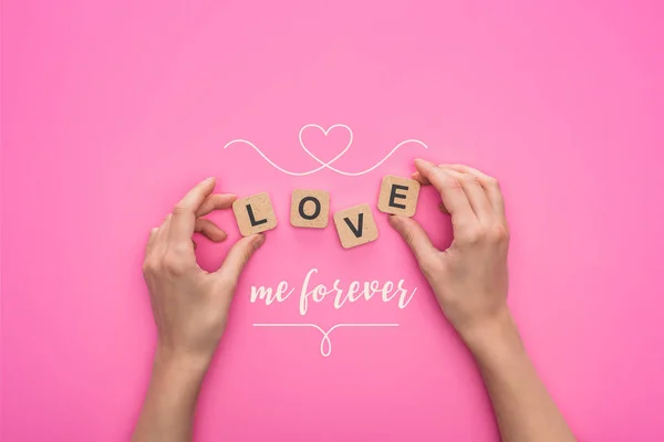 Partial view of woman holding cubes with love me forever lettering on pink background — Stock Photo