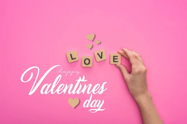 Partial view of woman holding cubes with love lettering on pink background with happy valentines day lettering — Stock Photo