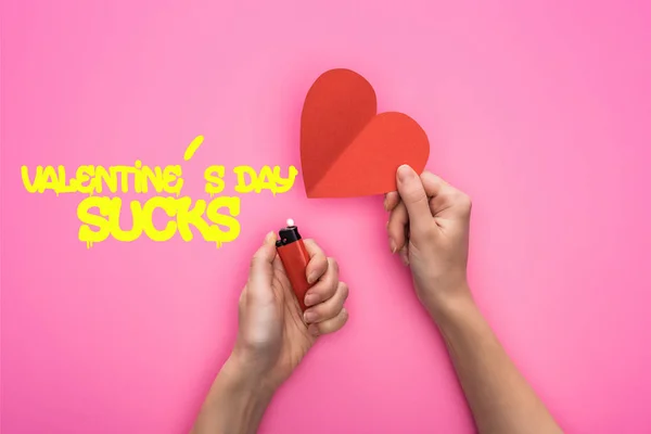 Cropped view of woman lighting up empty red paper heart with lighter isolated on pink with valentines day sucks illustration — Stock Photo