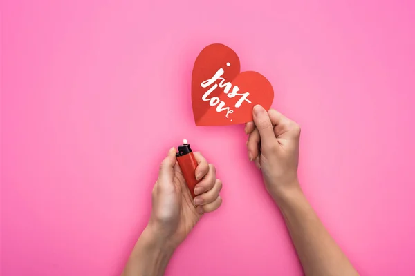 Vista cortada da mulher iluminando o coração de papel vermelho com letras de amor perto isqueiro isolado no rosa — Fotografia de Stock