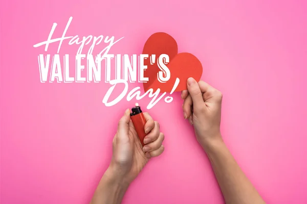 Vista cortada de mulher iluminando vazio coração de papel vermelho com isqueiro isolado em rosa com feliz dia dos namorados ilustração — Fotografia de Stock