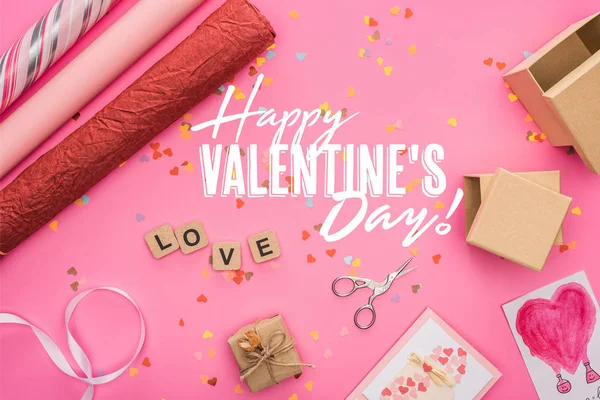 Top view of valentines confetti, scissors, wrapping paper, gift boxes, greeting cards and love lettering on wooden cubes on pink background with happy valentines day illustration — Stock Photo