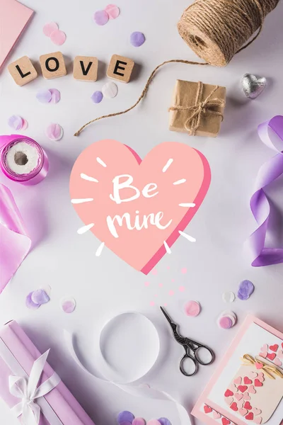 Ansicht von Valentinstagsdekoration, Geschenken, Bastelbedarf und Liebe Schriftzug auf Würfeln auf weißem Hintergrund mit be mine i heart Illustration — Stockfoto