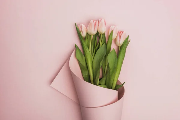 Vista superior de tulipanes envueltos en papel sobre fondo rosa - foto de stock