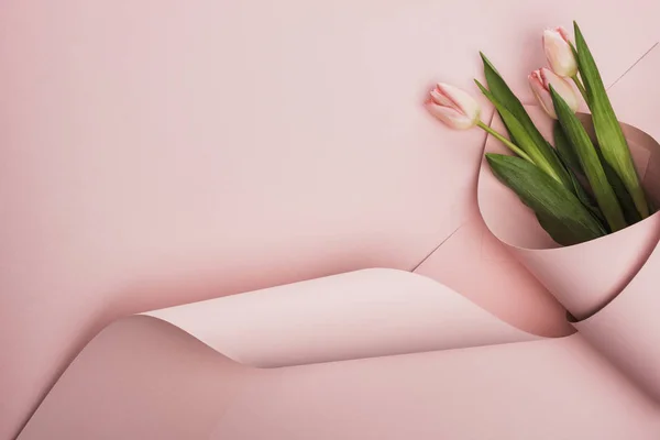 Vue du dessus des tulipes enveloppées dans du papier sur fond rose — Photo de stock