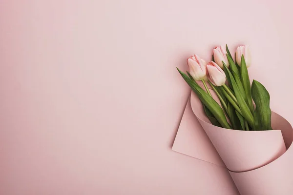Верхний вид тюльпанов завернутых в бумагу на розовом фоне — стоковое фото