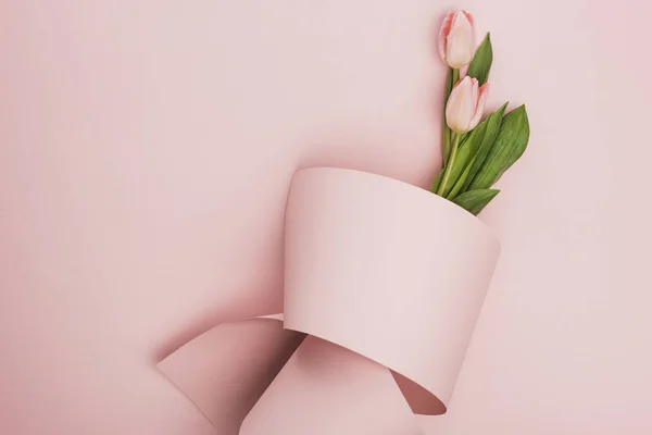 Vista superior del ramo de tulipanes envuelto en papel remolino sobre fondo rosa - foto de stock