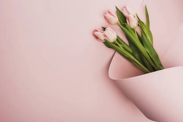 Vue du dessus du bouquet de tulipes enveloppé dans un tourbillon de papier sur fond rose — Photo de stock