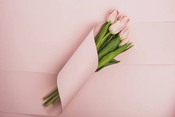 Top view of tulip bouquet wrapped in paper swirl on pink background — Stock Photo