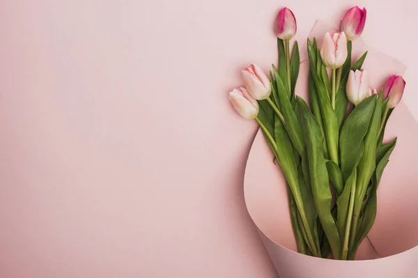 Vue de dessus des tulipes roses et violettes enveloppées dans un tourbillon de papier sur fond rose — Photo de stock