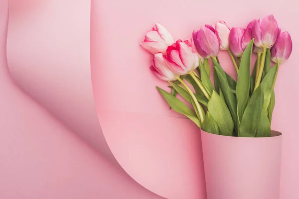 Vista superior de tulipanes envueltos en papel remolino sobre fondo rosa - foto de stock