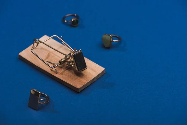 Close up view of jewellery rings with wooden mouse trap on blue background with copy space — Stock Photo