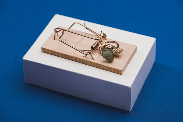 Anillo de joyería con piedra preciosa en trampa de ratón sobre bloque blanco sobre fondo azul - foto de stock