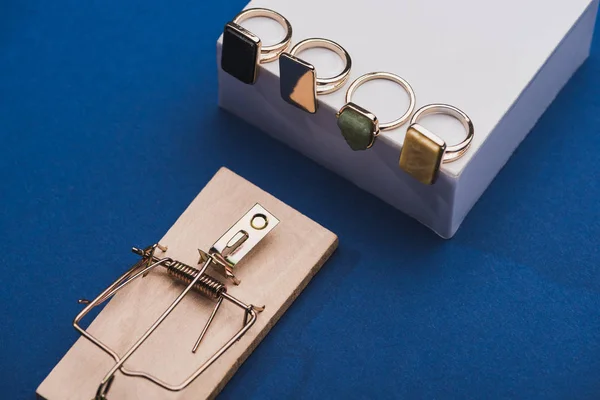Vista ad alto angolo di anelli di gioielleria su cubo bianco con trappola del mouse su sfondo blu — Foto stock