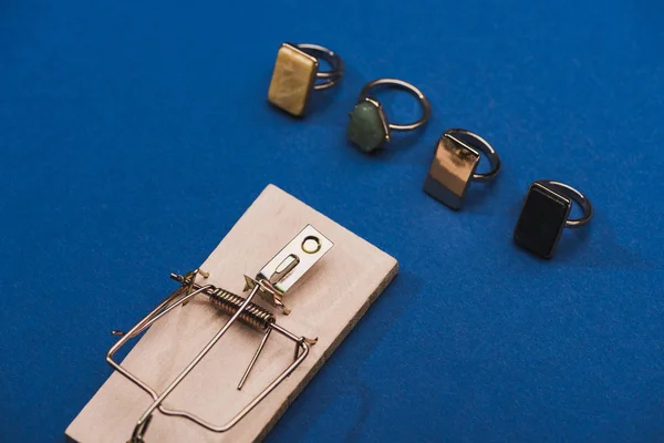 High angle view of wooden mouse trap with jewellery rings on blue background — Stock Photo