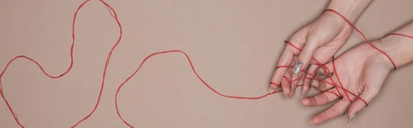 Top view of female hands with red string on beige background, panoramic shot — Stock Photo